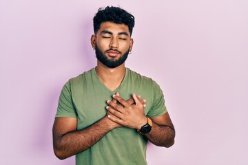 Sticker - Arab man with beard wearing casual green t shirt smiling with hands on chest, eyes closed with grateful gesture on face. health concept.