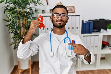 Poster - Young indian doctor holding support red ribbon pointing finger to one self smiling happy and proud