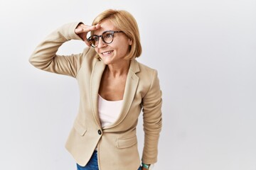 Poster - Middle age blonde business woman standing over isolated background very happy and smiling looking far away with hand over head. searching concept.