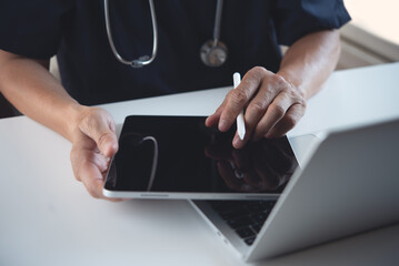 Wall Mural - Doctor using digital tablet and working on laptop computer on table at doctor's office in hospital. Sugeon recording patient's information on tablet, electronic medical record system