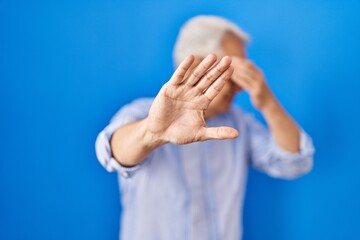 Sticker - Hispanic senior man wearing glasses covering eyes with hands and doing stop gesture with sad and fear expression. embarrassed and negative concept.