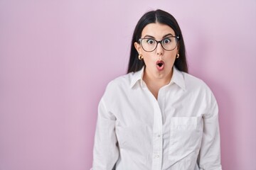 Wall Mural - Young brunette woman standing over pink background afraid and shocked with surprise expression, fear and excited face.