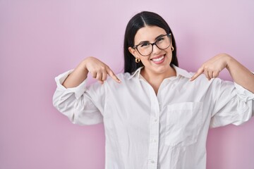 Poster - Young brunette woman standing over pink background looking confident with smile on face, pointing oneself with fingers proud and happy.