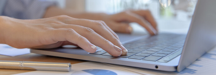 Wall Mural - Close-up of a woman's hand pressing on the laptop keyboard, World of technology and internet communication, Financial professionals use laptop to calculate and check real estate earnings.