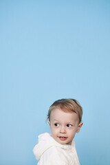 a little boy of 2 years sits in a white jacket on a blue background and thinks laughs happy sad sadness cheerful advertisement for children