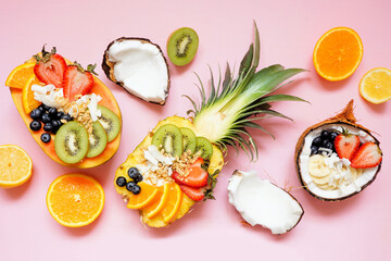 Wall Mural - Healthy fruit yogurt bowls in a pineapple, papaya and coconut. Above view table scene on a pink background.