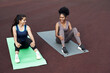 © etonastenka - Break in training. Two diverse young women are sitting on yoga mats in the stadium and talking, laughing.