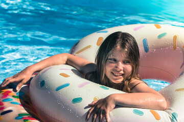 Wall Mural - pretty young girl playing with her donut-shaped buoy in the swimming pool