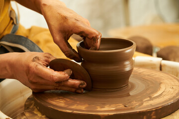 A Potter works with red clay on a Potter's wheel in the workshop..Women's hands create a pot. Girl sculpts in clay pot closeup. Modeling clay close-up. Warm photo atmosphere