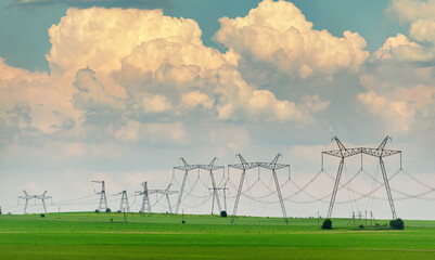 Wall Mural - Electric power lines on the countryside field with big clouds on the background.