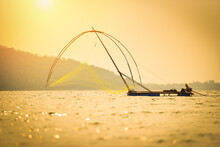 Asia Fisherman Net Using On Wooden Boat Casting Net Sunset Or Sunrise In The River - Silhouette Fisherman Boat With Mountain Island Background On The Sea Ocean