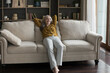 © fizkes - In warm living room beautiful single middle-aged woman leaned on sofa cushions looking carefree, enjoy weekend at modern fashionable home. Comfort untroubled living, cozy furniture, relaxation concept