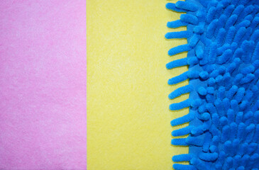 Pink, yellow and blue background. Fluffy blue floor cloth, pink and yellow dust cloth. Home cleaning.