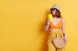 © sementsova321 - Indoor shot of dark haired beautiful woman in sunglasses wearing summer clothing posing isolated over yellow background, drinking cocktail, looking aside at copy space for advertisement.