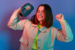 © sementsova321 - Portrait of joyful happy smiling woman wearing stylish jacket holding music column on her shoulder and dancing, listening music, posing isolated on neon light background.