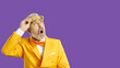 © Studio Romantic - Narrow shot of shocked old man in eccentric suit take off glasses surprised with deal or sale offer. Amazed mature male stunned with unbelievable promotion. Violet studio background. Copy space.
