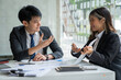 © crizzystudio - Two beautiful Asian businessmen working together in the office sitting at desk with a laptop working on paperwork to discuss the project's financial reports. business organization cooperation concept