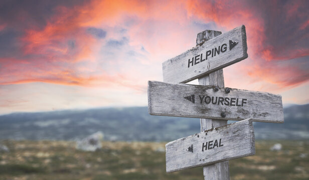 Wall Mural - helping yourself heal text quote caption on wooden signpost outdoors in nature with dramatic sunset skies. Panorama crop.