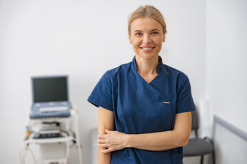 Wall Mural - Smiling doctor, ultrasound specialist looking at camera on her workplace in clinic