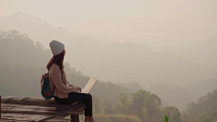 Wall Mural - Young woman freelancer traveler working online using laptop and enjoying the beautiful nature landscape with mountain view at sunrise