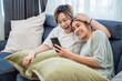 © somchairakin - Happy two lesbian woman, lgbtq homosexual Lesbian couples sharing earphones while listening music over smart phone in living room. Gay woman couple rest and relaxing by using smartphone in bedroom.