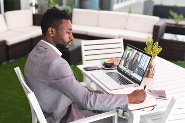 Poster - Serious african american businessman writing in diary while video conferencing over laptop in office