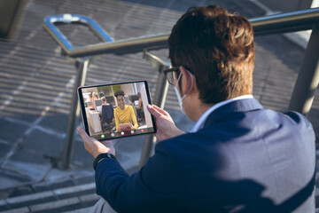 Wall Mural - Asian businessman wearing mask discussing over video conference on digital pc while sitting outdoors