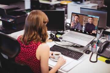 Poster - Caucasian businesswoman with coffee cup on desk video conferencing with coworkers over laptop