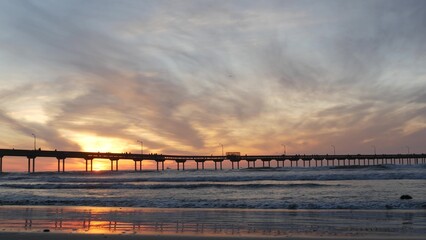 Wall Mural - Silhouette of people walking, pier on piles in sea water. Ocean waves and dramatic sky at sunset. California coast, beach or shore vibes at sundown. Summertime seascape. Seamless looped cinemagraph.