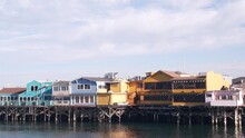 Colorful Wooden Houses On Piles, Pillars Or Pylons, Ocean Sea Water, Historic Old Fisherman's Wharf, Monterey Bay Or Harbor, California Coast USA. Tourist Beachfront Promenade, Waterfront Boardwalk.