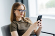 © F8  \ Suport Ukraine - Beautiful young woman holding phone and looking at camera with smile while sitting in big comfortable chair at home