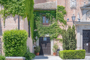 Front shot of an old house, focusing only on its roof and a barred window covered in green vegetation