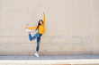 Joyful young asian woman dancing against concrete wall in the city