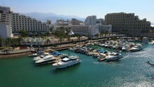 Aerial Panning Shot Of Famous Hotel Buildings In City, Drone Flying Over Sea On Sunny Day - Eilat, Israel