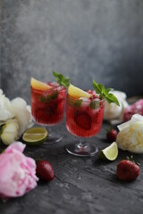 Refreshing strawberry lemonade with lemon basil, lime and ice. Two glasses with cold berry cocktail.