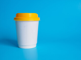 Wall Mural - Front top view, white coffee paper cup yellow lid, filled with hot black coffee(americano), no sugar milk, ready to drink, refreshing. aroma awake fresh to work placed on  Blue isolated background
