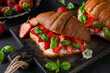 French croissant sandwiches with fresh strawberries, soft cheese and basil on black background. Tasty breakfast