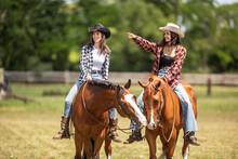 Two Good-looking Young Women Ride Their Horses, One Pointing To The Right While Horses Touch With Lips