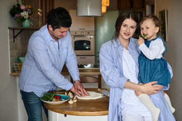 dad mom and their daughter cook pizza together in the kitchen. T