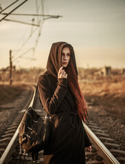 Young lonely woman walking along railway track, on background of industrial city, in dramatic and anti-utopia style