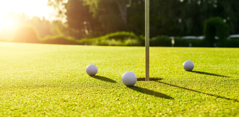 Wall Mural - Three golf balls on the green grass near hole on a golf course at sunset