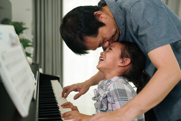 Wall Mural - Asian father kissing daughter and smiling together with happy moment while playing piano at home,concept of love, bonding, relation, education, music, skill, mental health, parent and child in family 