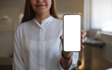 Mockup image of a young woman holding and showing a mobile phone with blank white screen