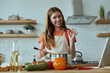 © gstockstudio - Confident young woman cooking soup and gesturing while standing at the domestic kitchen