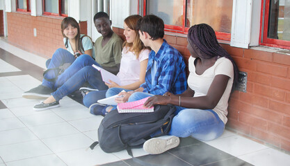 Wall Mural - Multi ethnic schoolmates sitting in the school hallway relaxing and doing school lesson