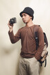 Portrait of young asian boy wearing black hat gesturing taking picture with camera and carrying backpack
