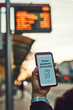 © Przemek Klos - Woman buying ticket online near bus stop before ride. Person paying for ticket using mobile payment app. Using technology on the go. Order confirmation on mobile screen. Top up account in app