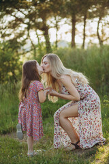 Wall Mural - Happy family on a summer meadow. little girl child daughter hugging and kissing mother