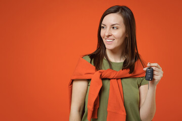 Wall Mural - Young smiling happy woman 20s wearing khaki t-shirt tied sweater on shoulders look aside on workspace area hold car keys remote fob keyless system isolated on plain orange background studio portrait