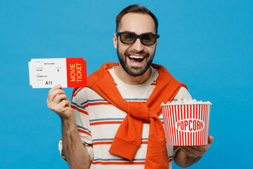 Wall Mural - Young fun smiling happy cheerful cool man in 3d glasses watch movie film hold bucket of popcorn hold ticket look camera isolated on plain blue background. People emotions in cinema lifestyle concept.